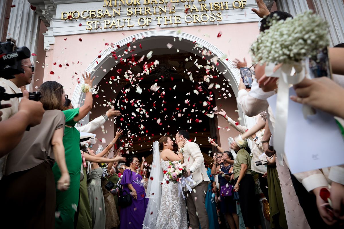 Newlyweds kissing beneath a shower of petals as guests cheer outside the church