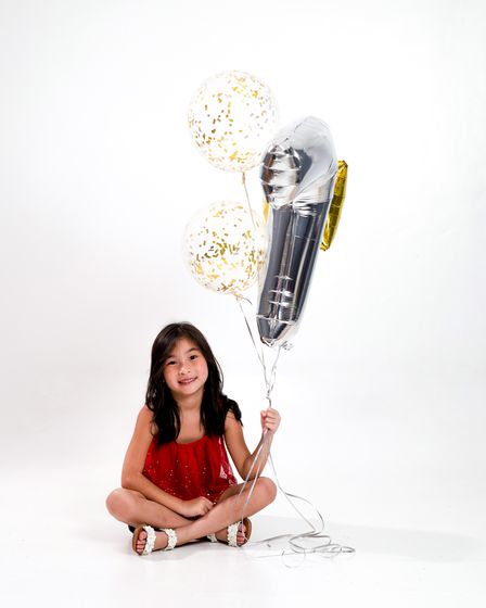 A girl in red seated on the floor holding a number balloon
