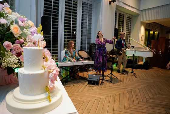 A tiered floral cake beside a live band at a party venue