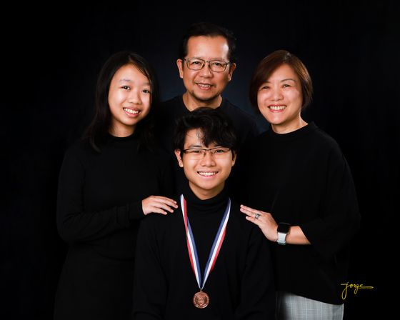 A family of four in matching black against a dark studio backdrop