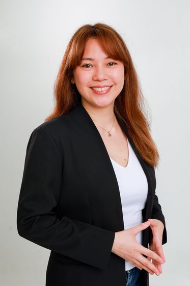 A woman in a black blazer, hands clasped