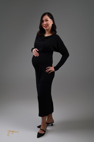 An expectant mother in a black dress, hand on her waist